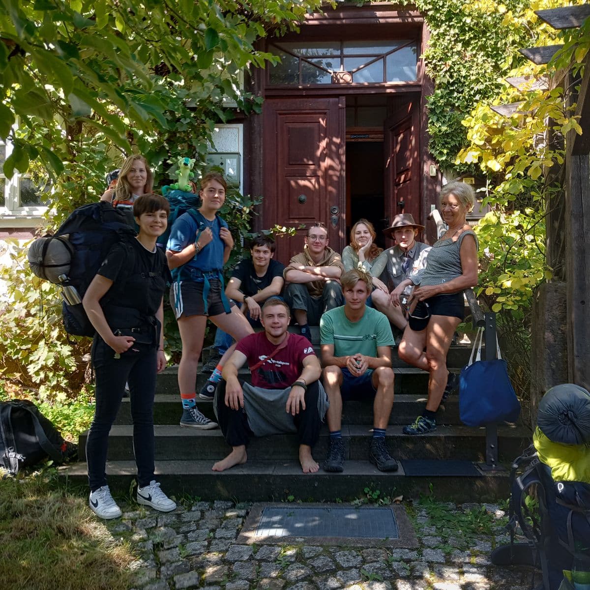Gruppe vor einem Eingang im Grünen, mit Rucksäcken.
