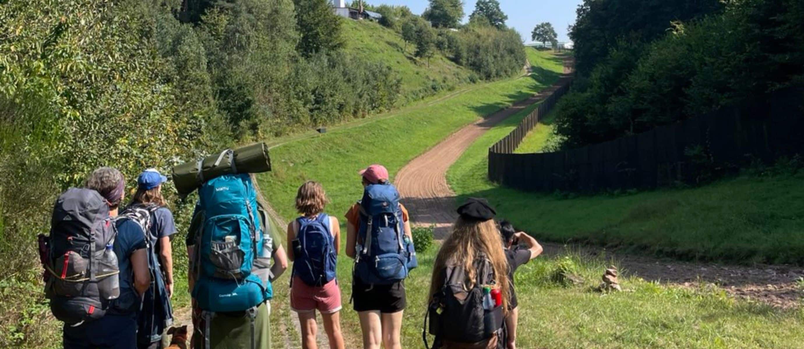 Gruppe Wandert mit Rucksäcken einen Waldweg hinauf.