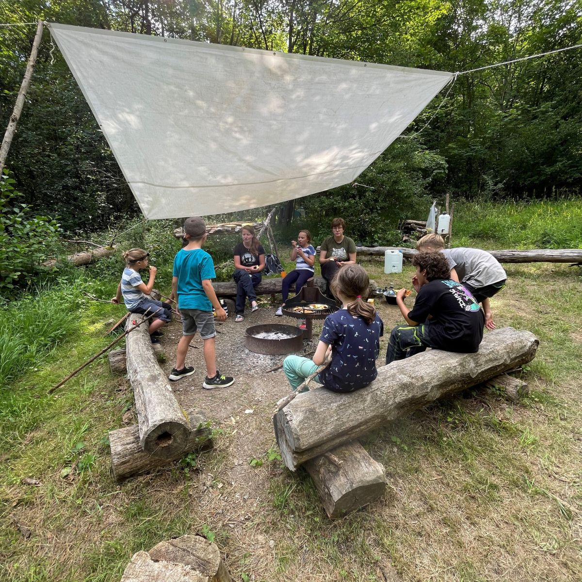 Kinder im Wald sitzen um Lagerfeuerplatz.