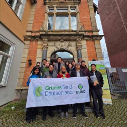 Gruppe mit Banner vor einem Gebäude während Treffen.