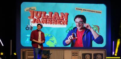 Mann auf Bühne vor bunter Plakatwand.